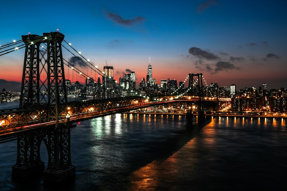 Illuminated suspension bridge and Manhattan skyline across the waterfront at dusk